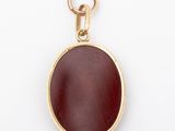 a close up of a gold and red pendant on a white background