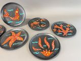 four plates with orange and blue designs on them sitting on a white surface