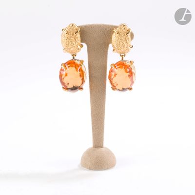 une paire de boucles d'oreilles ornées de pierres orange, présentées sur un support, sur fond blanc