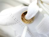 a close up of a pair of white shoes with a gold button