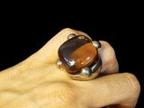 la main d'une personne tenant une bague sertie d'une pierre « œil-de-tigre »