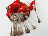 tomatoes in a bowl with forks and spoons on a white surface