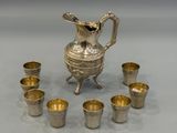 an image of a silver pitcher and six cups on a table