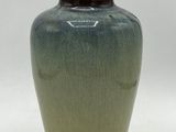 un vase vert avec un couvercle noir posé sur une surface blanche