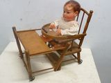une poupée assise dans une chaise haute sur laquelle est posé un plateau