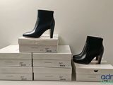 two pairs of black high heeled boots sitting on top of a stack of white boxes