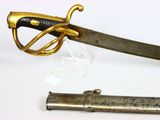 a gold colored sword with a black handle on a white surface