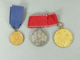three medals are shown on a gray surface with a red ribbon