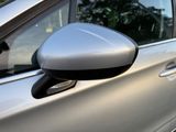 the side view mirror of a silver car with trees in the background
