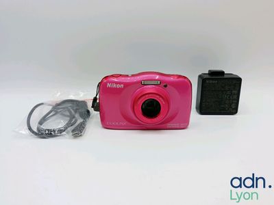 une photo d'un appareil photo numérique rose posé à côté d'un chargeur