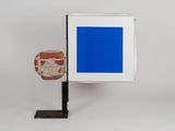 a blue square on a black stand next to a brick wall