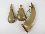 trois bouteilles en verre et une corne posées sur une surface blanche
