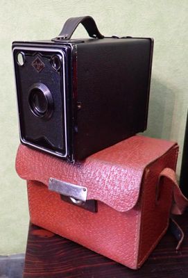un petit appareil photo marron posé sur une valise rouge