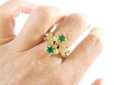 a woman ' s hand holding a gold ring with green stones
