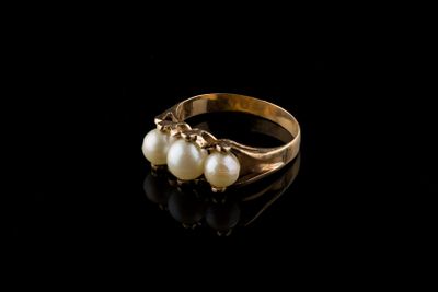 un gros plan d'une bague en or ornée de perles sur un fond noir
