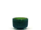 un bol vert posé sur une surface blanche, sur fond blanc