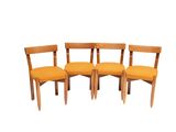 three wooden chairs with orange cushions sit side by side on a white surface