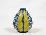 un vase jaune et bleu posé sur une surface blanche
