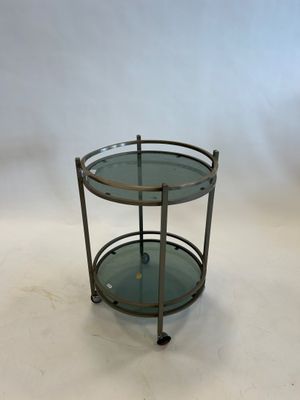 une table ronde en verre avec un piètement en métal et deux étagères