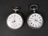deux montres de poche en argent posées côte à côte sur une surface noire