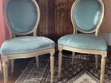 pair of blue upholstered chairs sitting on a rug in front of a wooden cabinet
