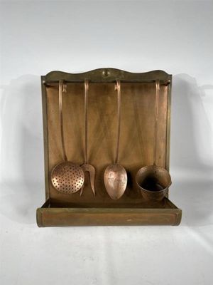 ustensiles et cuillères en laiton présentés dans une vitrine sur fond blanc