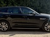 the black car is parked on the gravel road in front of the bushes