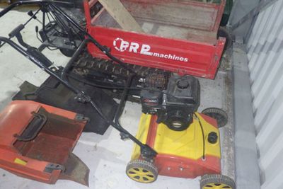 deux tondeuses à gazon posées par terre à côté d'un chariot rouge