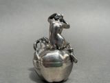 a silver figurine of a woman sitting on top of an apple
