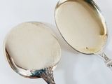 two silver spoons sitting next to each other on a white surface