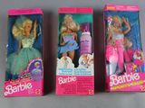three barbie dolls are in their boxes on a gray surface