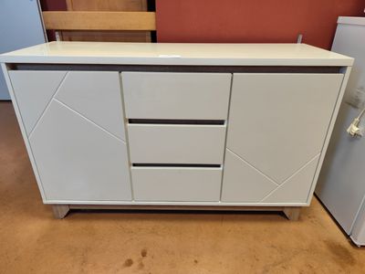 une armoire blanche à tiroirs, avec un réfrigérateur en arrière-plan