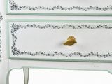 a white chest of drawers with green trim and a gold knob