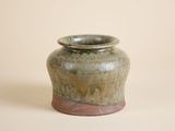 un petit vase vert avec un socle marron sur un fond blanc