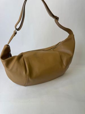 the large tan leather bag is sitting on a white surface