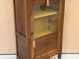 a small wooden cabinet with a glass door and a tassel on the door