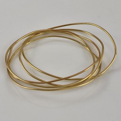 four gold colored wire bracelets stacked on top of each other on a white surface