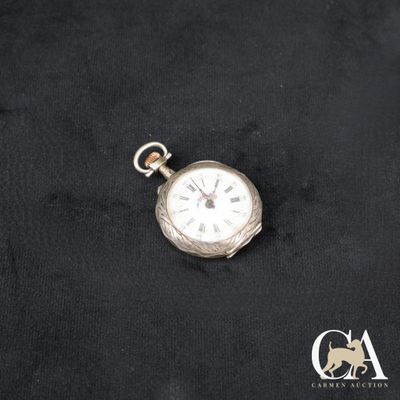 une image représentant une montre de poche en argent posée sur un tissu noir