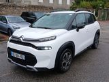 La petite voiture blanche est garée sur le parking, à côté d'autres voitures.