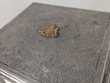 an old silver box sitting on a white surface with a gold emblem on it
