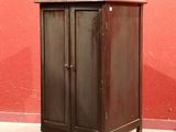 une petite armoire dans un coin d'une pièce, avec un mur rouge en arrière-plan
