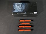 three orange pens sitting on top of a black table next to a box of ink