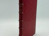 an old red book sitting on top of a table next to a white wall