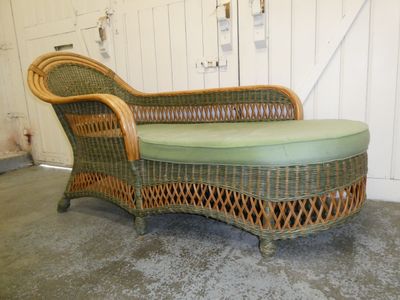 a wicker chaise with a green cushion on it