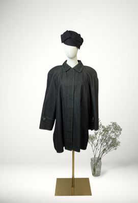 mannequin with a black coat and hat on a stand next to a vase of flowers