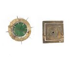 two pieces of metal and a green stone on a white surface