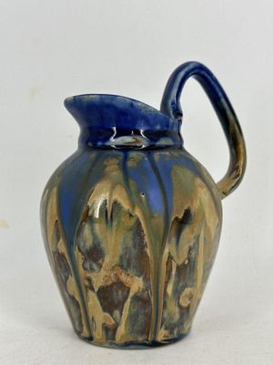 un vase bleu et marron muni d'une anse, posé sur une surface blanche