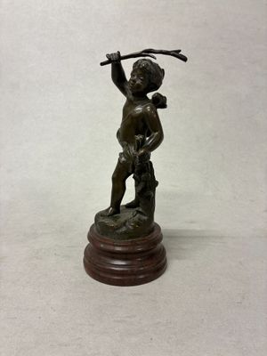 figurine en bronze représentant un garçon tenant un bâton, posée sur un socle en bois