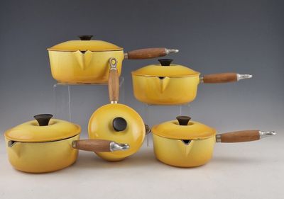 plusieurs casseroles et poêles jaunes munies de poignées en bois, posées sur une table