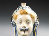 un petit vase orné d'un visage, posé sur un socle